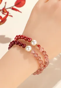 Detail shot of layered red cinnabar and translucent agate bracelets with white pearls.