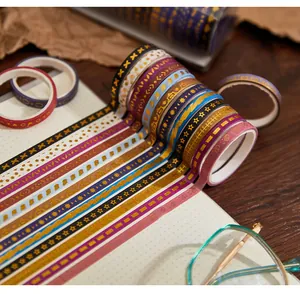 Close-up of decorative gold foil washi tape rolls with various patterns on a notebook.