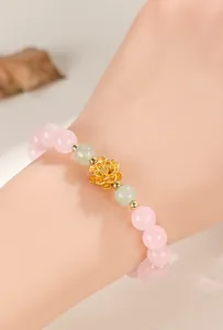 Close-up view of a pink and green beaded bracelet featuring a gold lotus charm on a wrist