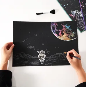 Nahaufnahme von Händen, die ein DIY-Weltraum-Kratzbild mit Astronautenmotiv erstellen
