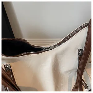Detailed macro view of white faux leather tote bag with silver zippers and brown shoulder straps.