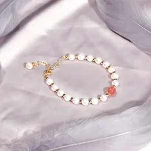 Elegantes weißes Perlenarmband mit einer rosa Edelsteinperle auf weichem Federhintergrund