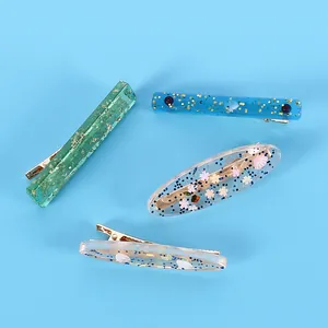 Détail rapproché de quatre barrettes en résine faites main avec paillettes et petites fleurs.