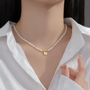 Detail view of a seed pearl necklace with a gold 'M' initial pendant on a model.