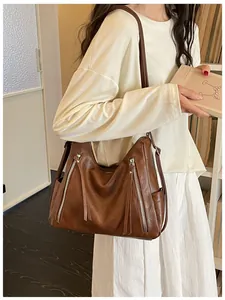 Close-up of a large brown faux leather underarm bag with decorative tassel zippers
