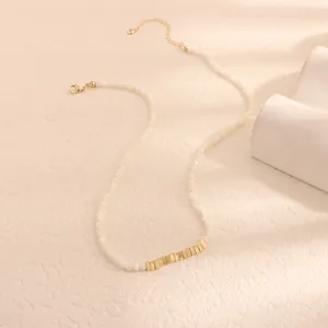 Macro dettaglio di una collana di perline in conchiglia bianca con accenti dorati rettangolari.