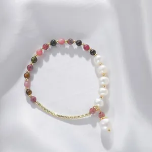 Elegantes Perlenarmband mit weißen Perlen und bunten Steinen auf weißem Stoff.