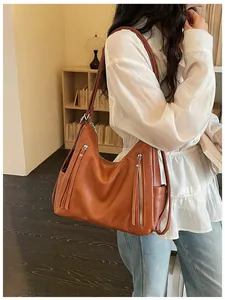 Stylish brown faux leather shoulder bag with zipper tassel details shown on a model.