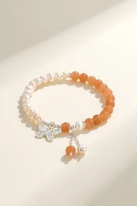 Close-up of handmade freshwater pearl and orange agate bracelet with butterfly charm