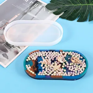 Detail view of an oval silicone tray mold shown next to a pearl-decorated resin coaster
