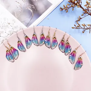 Close-up of colorful gradient cicada wing earrings with rhinestones on a pink plate