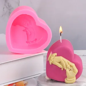 Close-up of pink heart silicone mold next to a lit holding hands candle on marble plate