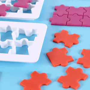 Close-up of white puzzle shape cookie cutters and colorful fondant puzzle pieces
