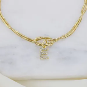 Detailansicht eines goldenen Schlangenknoten-Armbands mit einem kristallbesetzten E-Anhänger