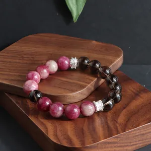 Primer plano de pulsera de cuentas de turmalina rosa y cuarzo ahumado en soporte de madera.