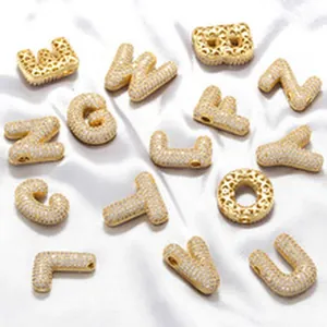 Detail view of gold micro-pave alphabet beads scattered on white satin fabric.
