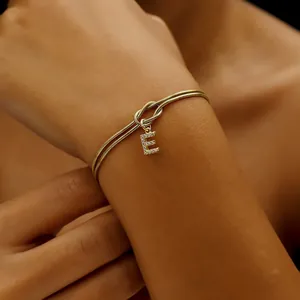 Nahaufnahme eines goldfarbenen Schlangenkette-Armbands mit kristallinem Buchstaben E