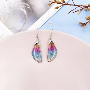 Macro view of gradient cicada wing earrings with silver glitter accents and hooks.