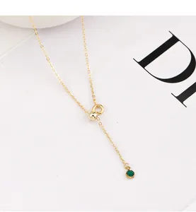 Close-up detail of a delicate gold Y-shaped necklace with sliding bead and green gem pendant.
