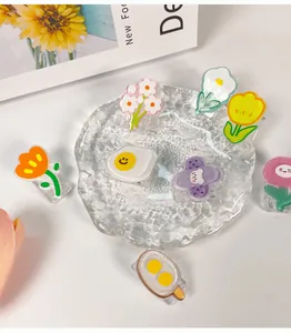 Detailansicht süßer Cartoon-Acrylclips in Blumen- und Eiformen auf einer Glasplatte
