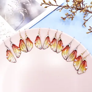Gradient cicada wing drop earrings with sparkling rhinestones arranged on a pink plate