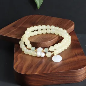 Detailansicht eines zweisträngigen gelben Edelsteinarmbands mit weißem Jade-Ananhänger.