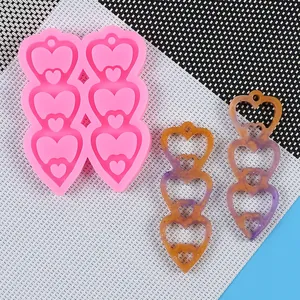 Triple heart silicone earring mold with resin pendant samples on a mesh mat background