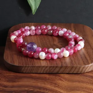 Detail van een dubbele armband met roze kristallen kralen en zoetwaterparels op hout.