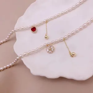Gros plan de colliers en perles d'eau douce avec pendentifs cœur et fleur en zircon