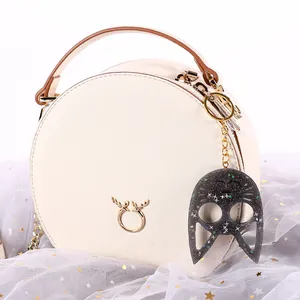 Detail view of a glittery cat head keychain on a white round leather crossbody bag