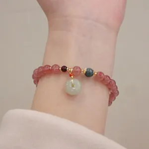 Dettaglio di un braccialetto di perle rosa con un ciondolo in giada verde su un polso.