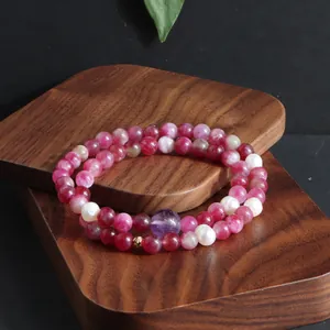 Gedetailleerde weergave van de dubbele armband met roze toermalijn en parels op hout.