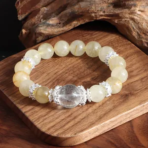 Detalle de pulsera de cuarzo rutilado dorado con adornos plateados sobre madera.