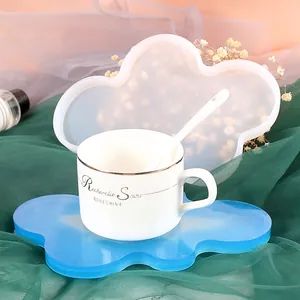 Cloud shaped silicone coaster mold shown with finished blue resin piece and white coffee cup