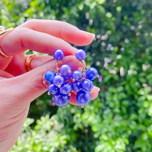 Close-up view of elegant purple grape cluster pearl earrings held by hand in a sunny garden