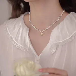 Detalle de un collar de perlas barrocas con colgante dorado 'Good Luck' en una modelo.