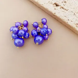 Macro detail of vibrant purple grape cluster pearl earrings on natural stone background