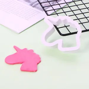 Detaillierte Ansicht einer weißen Einhorn-Plätzchenform aus Kunststoff und rosa Teig auf Grün.