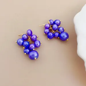 Detail view of purple grape-shaped cluster pearl earrings on a neutral background.