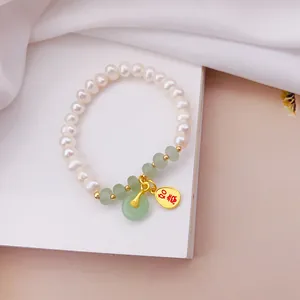 Dettaglio del bracciale con perle bianche, pietre di giada e ciondolo portafortuna d'oro