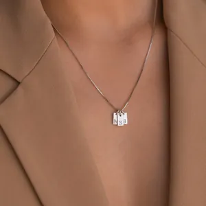 Detailansicht einer silbernen Halskette mit drei kleinen, gravierten Buchstaben-Anhängern.