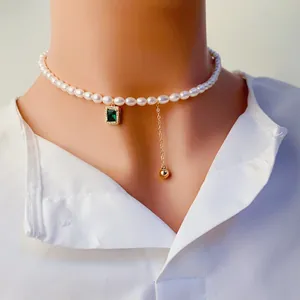 Gros plan du ras-du-cou en perles avec pendentif zircon vert émeraude et pompon