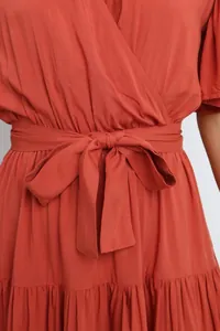 Detail view of the elegant front waist-tie bow on a terracotta Bohemian V-neck wrap dress
