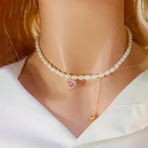 Détail du collier ras du cou en perles d'eau douce avec pendentif cœur rose et gland doré.