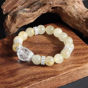 Primer plano de una pulsera de cuarzo rutilado dorado con dijes de corona sobre madera.