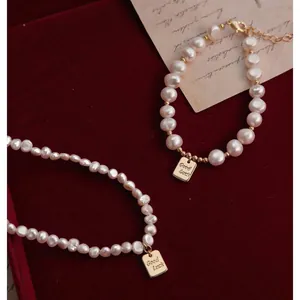 Primer plano de collar y pulsera de perlas barrocas con colgante de oro Good Luck