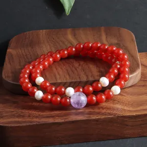 Detailweergave van een dubbele armband met rode kralen, parels en paarse amethiststeen.