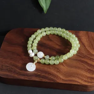Detailansicht eines zweireihigen grünen Perlenarmbands mit Perlen und rundem Anhänger.