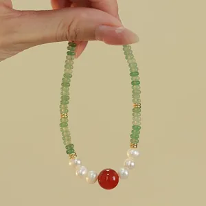 Close-up detail of aventurine and pearl necklace with a central red agate bead.