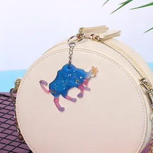 Detail of a sparkling blue and pink resin Taurus zodiac keychain on a beige bag